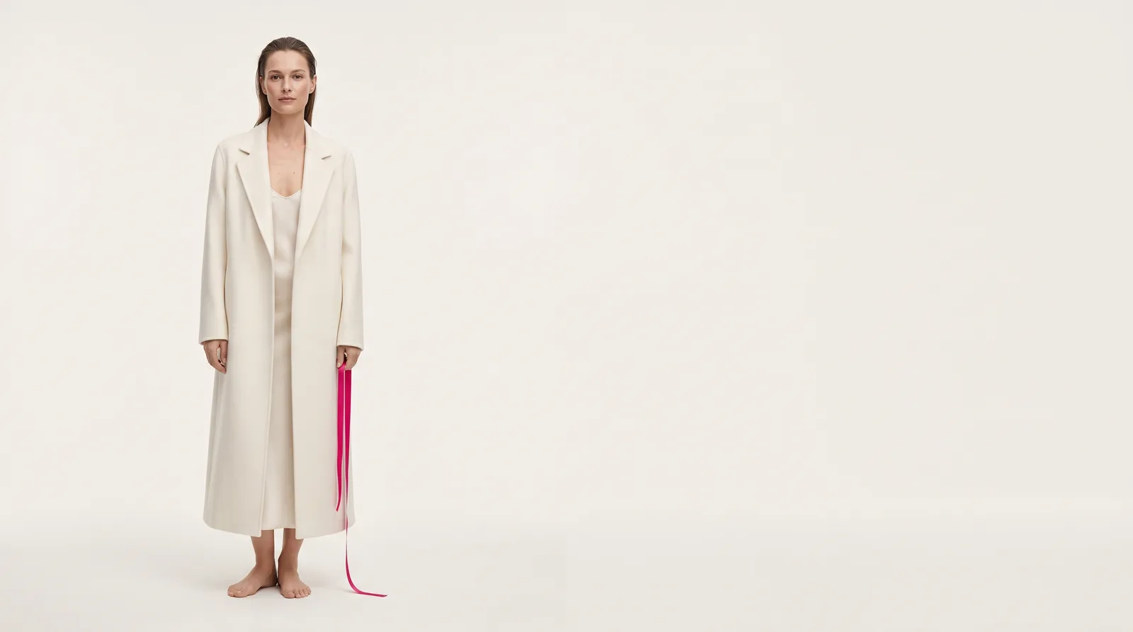 A model in a long cream coat, a magenta ribbon in her hand
