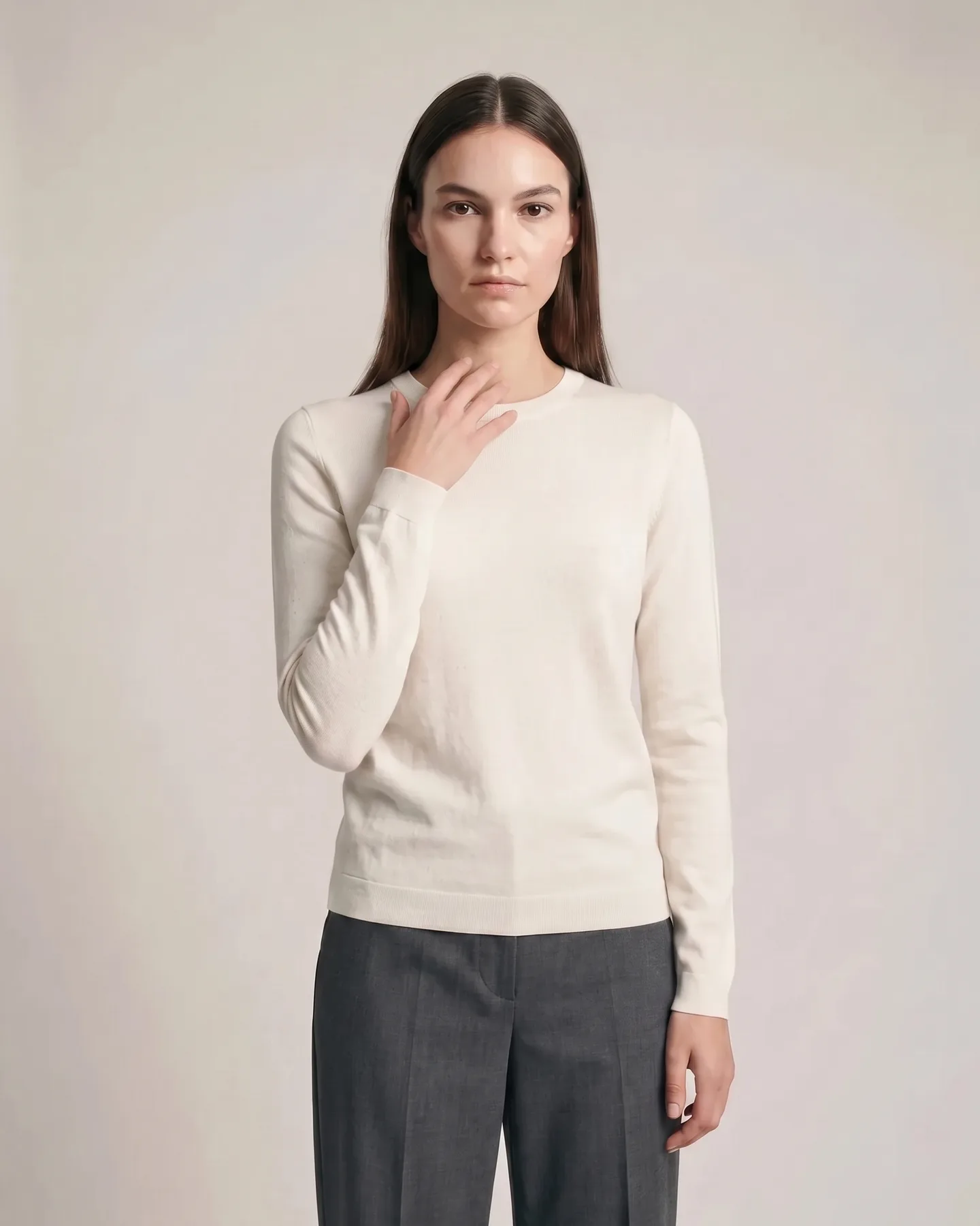 One hand lifted to the collarbone, the knit sleeve gathering at the wrist