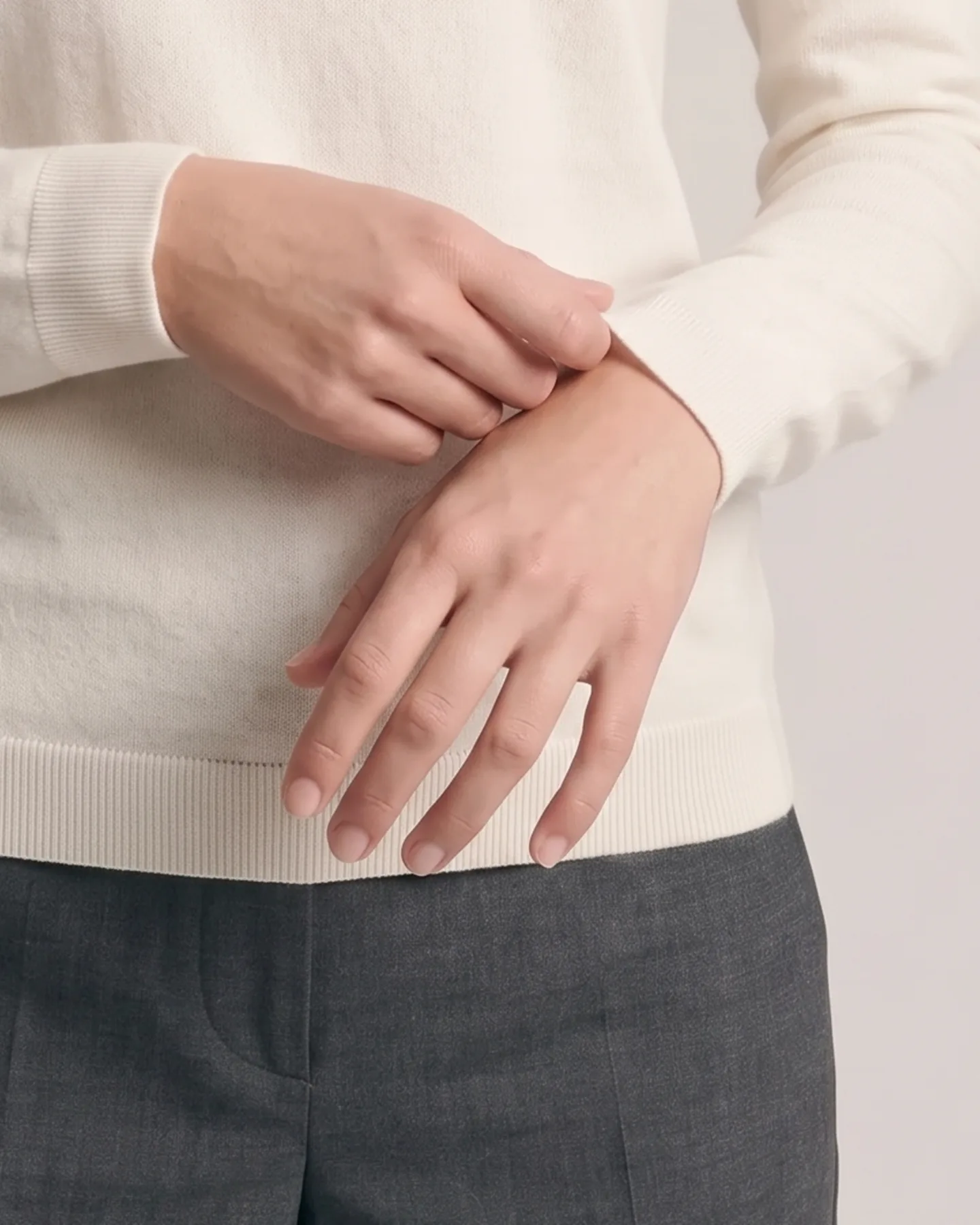 Both hands at rest against the ribbed hem, the sleeve pushed clear of the wrist