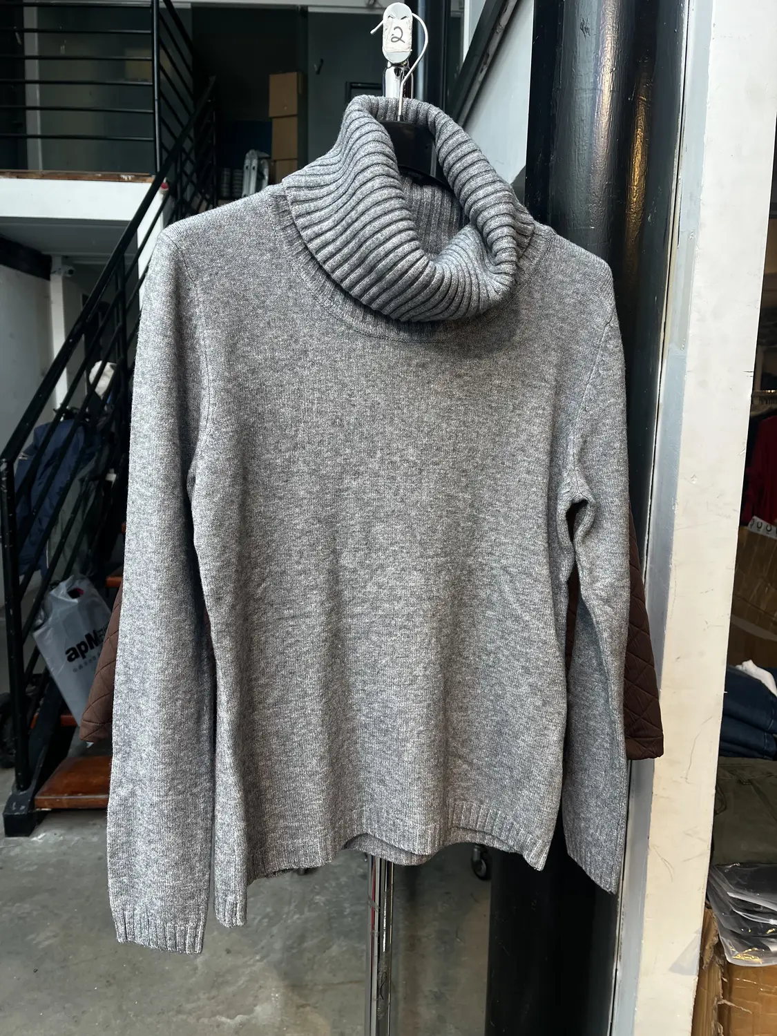 A grey roll-neck jumper on a hanger in a stockroom, photographed on a phone